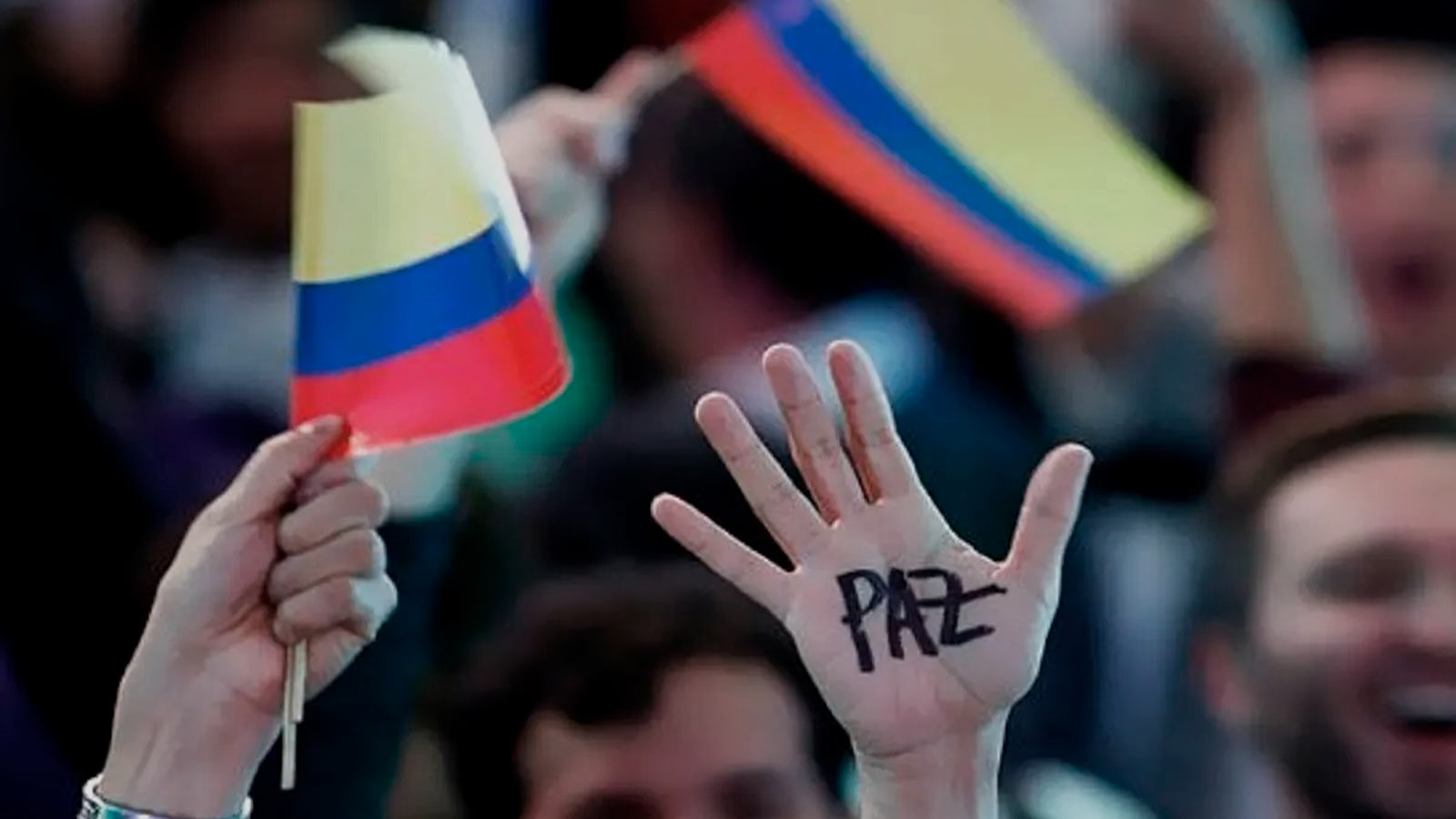 Persona levanta la mano con la palabra paz junto a banderas de Colombia.