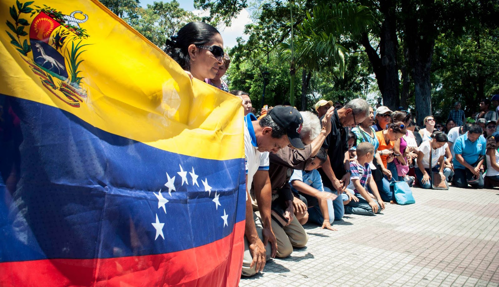 Personas orando junto a una bandera de Venezuela.